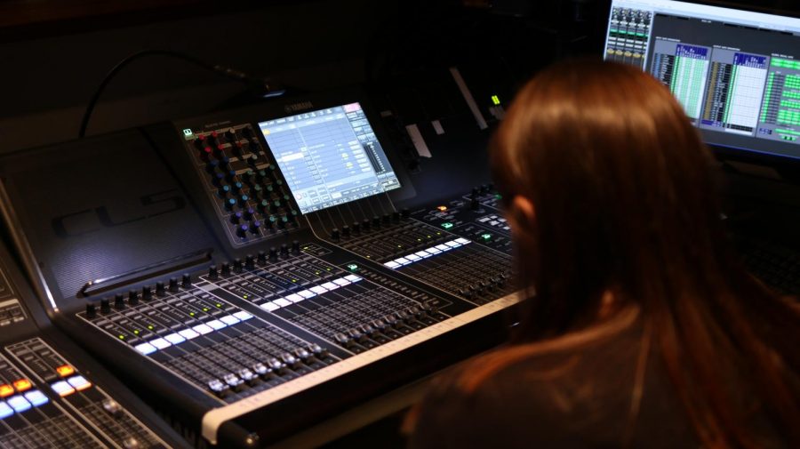 Macy Rothermel sits at the sound board in the auditorium booth during a tech week rehearsal.