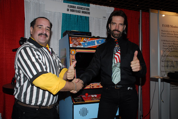 Billy Mitchell shakes hands with Todd Rogers--a former Twin Galaxies referee who has since been banned for similar cheating scandals--at the 2007 Florida Association of Mortgage Brokers Convention; the joystick with questionable authenticity  is in plain view behind them. 