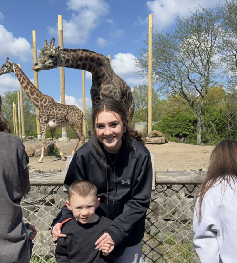 NASH+senior+Libby+Herne+and+a+preschool+student+pose+in+front+of+giraffe+exhibit.+